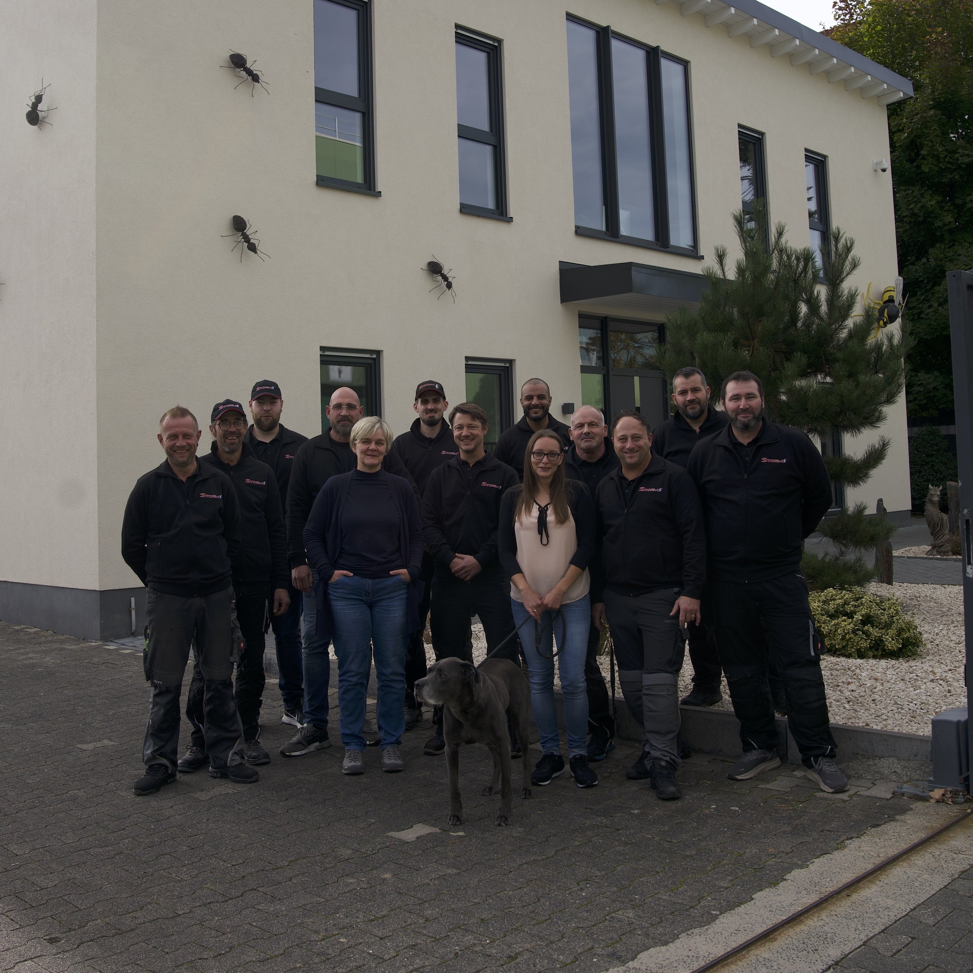 Ein helles, geräumiges Firmengebäude der Storm Schädlingsbekämpfungs GmbH, vor dem ein Team aus engagierten Mitarbeitern, mehrheitlich männlich, in Firmenuniformen posiert.