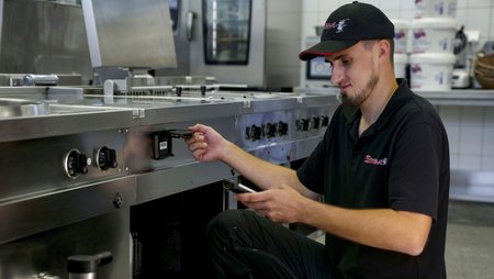Ein STORM GmbH Mitarbeiter scannt mit einem Handheld-Scanner einen Barcode auf einen Edelstahlschrank in einer Gastronomischen Küche ab.