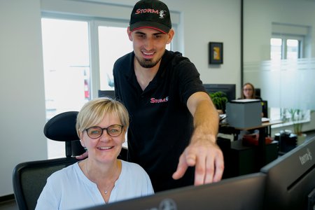 Ein Mann und eine Frau, beide lächelnd, in einer Büroumgebung der STORM GmbH, zeigen Teamarbeit an einem Computerarbeitsplatz