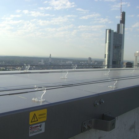 Flaches Dach mit drei Reihen von paarigen Edelstahlschienen, die darauf verlegt sind. Im Hintergrund sieht man die Skyline Frankfurt.