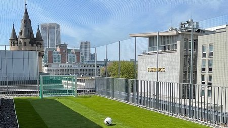 Frankfurter Dachterrasse eines Hochhauses mit gepflegter Rasenlandschaft, Fußballtor und Ball, das von einem maßangefertigten Schutznetz eingerahmt wird.