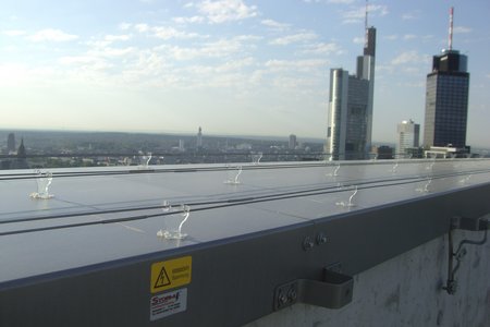Flaches Dach mit drei Reihen von paarigen Edelstahlschienen, die darauf verlegt sind. Im Hintergrund sieht man die Skyline Frankfurt.