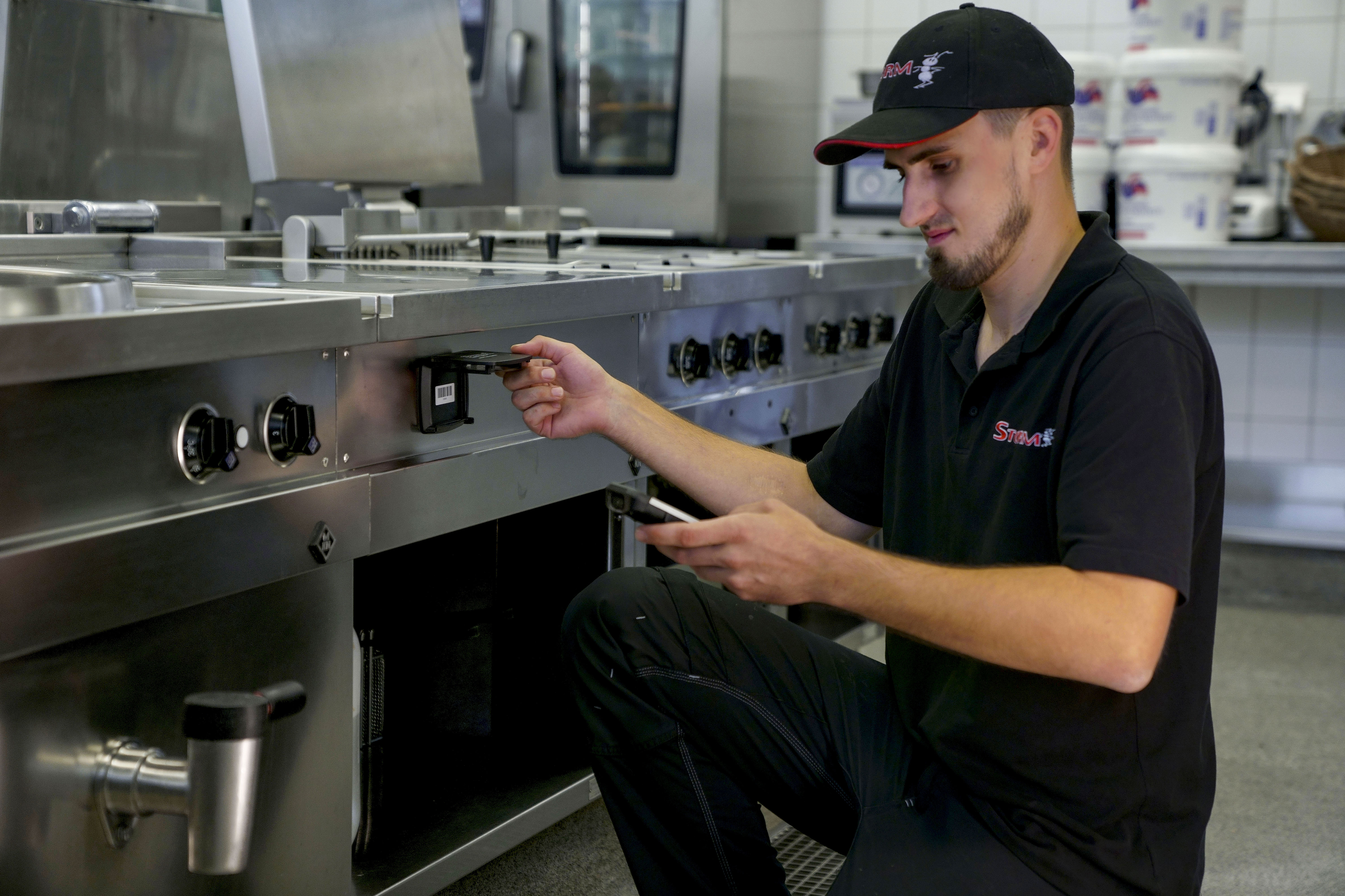 Ein STORM GmbH Mitarbeiter scannt mit einem Handheld-Scanner einen Barcode auf einen Edelstahlschrank in einer Gastronomischen Küche ab.